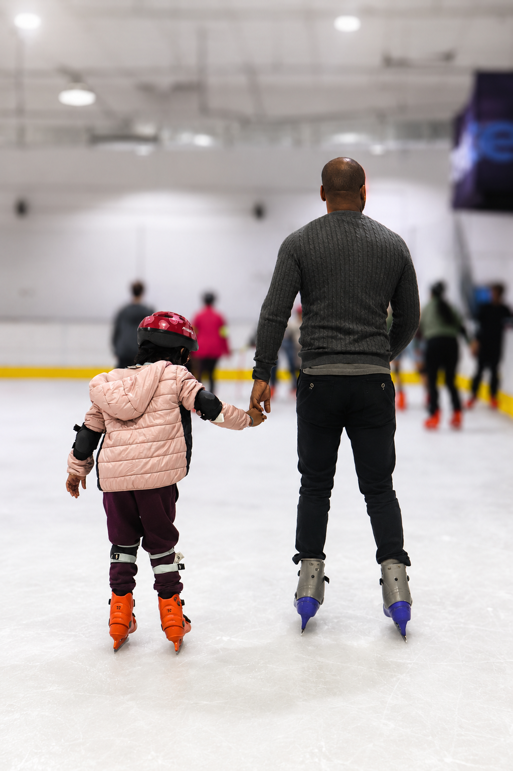 Pai e filha de mãos dadas na pista de gelo